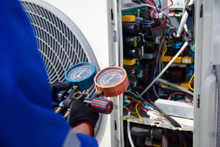 The air conditioner technician is using a gauge to measure the refrigerant pressure