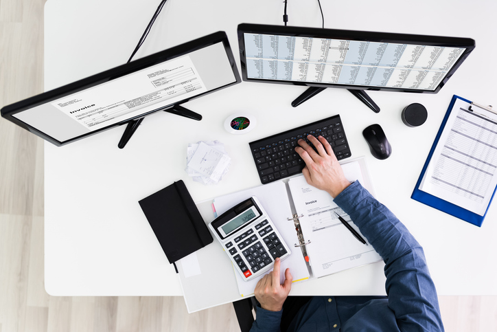 Young Businessman Calculating Bill With Computer And Laptop On Desk