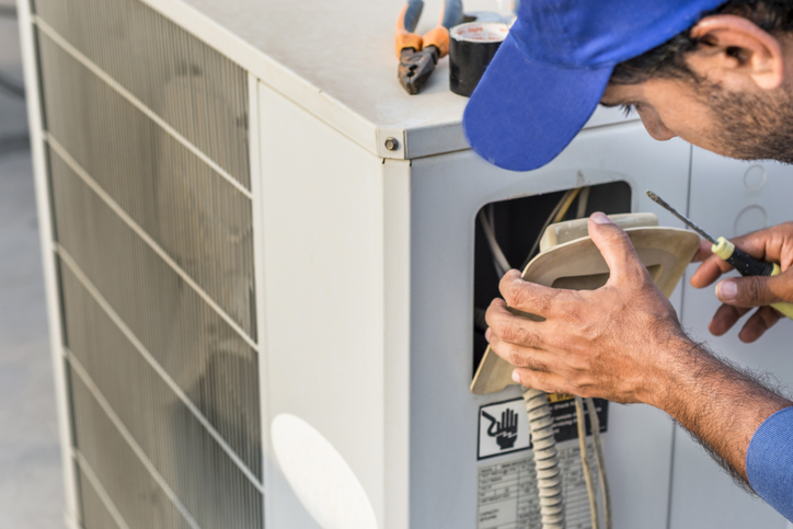 a professional electrician man is fixing the heavy unit of an air conditioner at the roof top of a building and wearing blue uniform and head cap