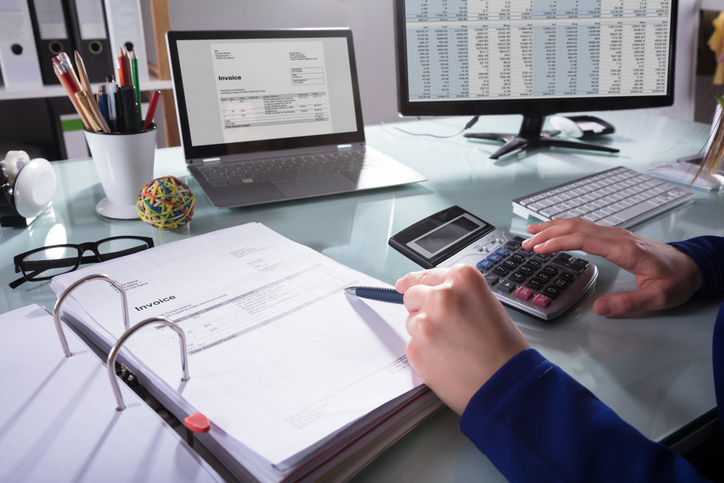 Close-up Of A Businessperson's Hand Calculating Invoice At Workplace