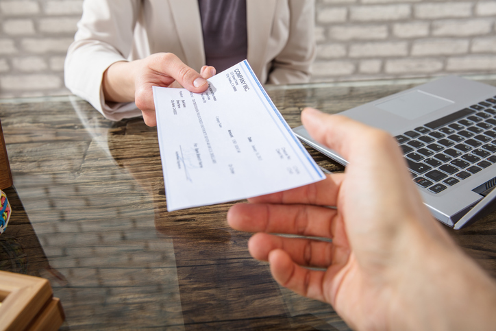 Close-up Of A Business Woman Giving Cheque To Her Colleague At Workplace In Office