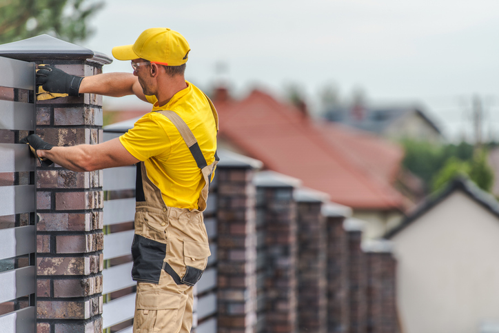 Brick and Wooden Panels Residential Home Fence Building by Professional Caucasian Construction Worker.