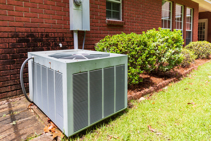 Older style air conditioner system next to home, brick and bushes with clean yard