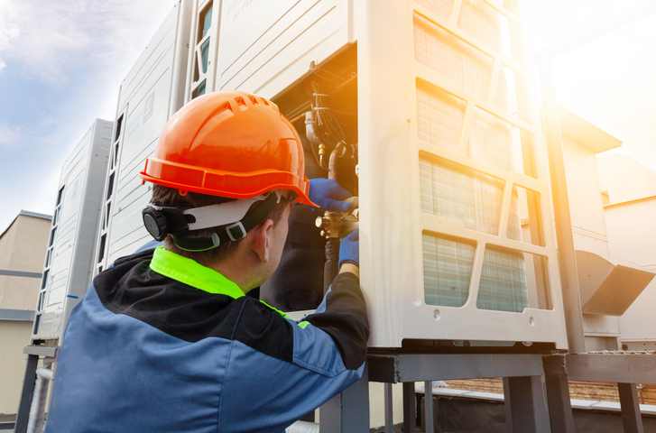 two people repairing an industrial air conditioner