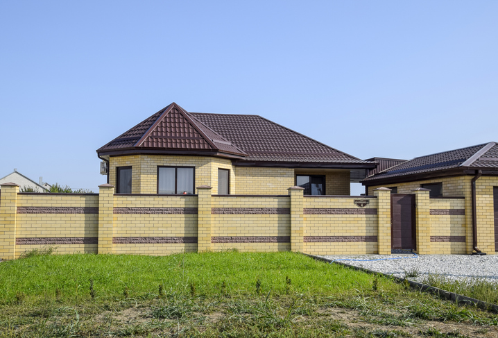 View of a new built-up fence material comparison and a house made of bricks and corrugated metal