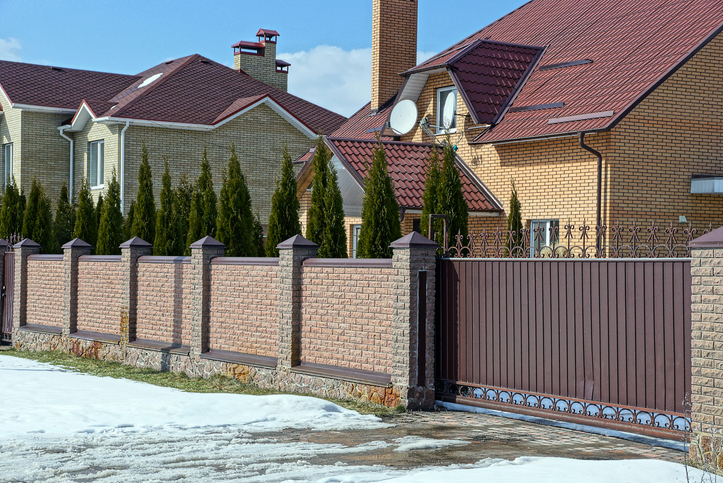 Brown brick fence material comparison and iron closed gates on the street near the road in the snow