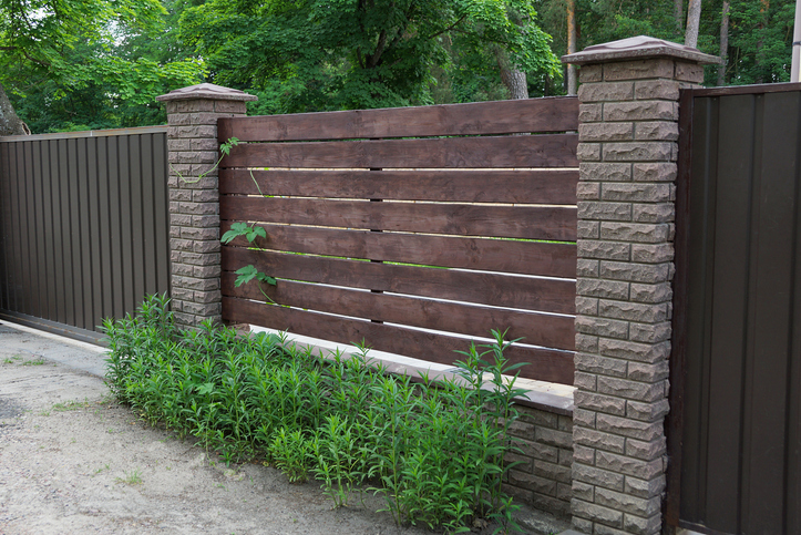 brown fence made of wooden planks and bricks in the green grass