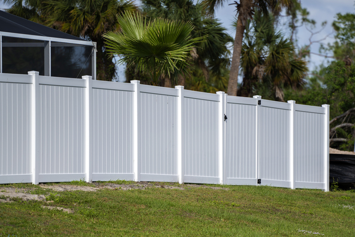 White vinyl picket fence on green lawn surrounding property grounds fadvantages of installing a privacy fence or backyard protection and privacy